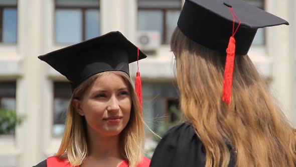 Blond Woman in Academic Cap Listening to Best Friend at Graduation Ceremony