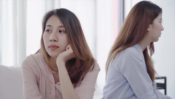 Asian lesbian lgbt couple sitting each side of sofa with moody emotion in living room.