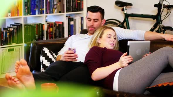 Couple using mobile phone and digital tablet on sofa