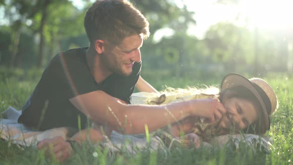 Joyful Man Laughing Tickling Girl Lying in Sunbeam on Spring Summer Lawn in Park