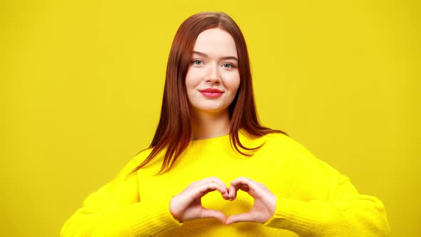 Happy Young Redhead Woman Showing Heart Shape with Hands Looking at Camera Smiling