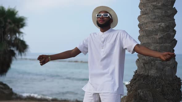 Medium Shot of Dancing Bearded African American Man with Blue Waves of Mediterranean Sea Rolling in