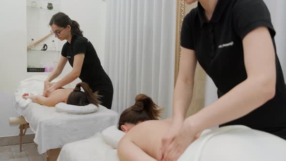 Female therapist massages a young woman on her back and shoulders. Relaxing massage.