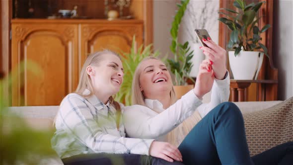 Two Positive Energetic Women Taking Selfie Photo on a Sofa in Luxury Modern Living Room