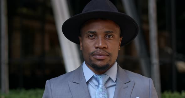 Portrait of Stylish Guy in Hat and Suit Looking To Camera While Standing at Street, Close Up View 