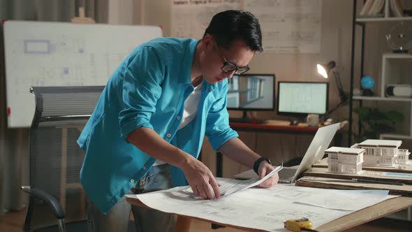 Asian Man Engineer With A Laptop Looking At Blueprint While Working At The Office