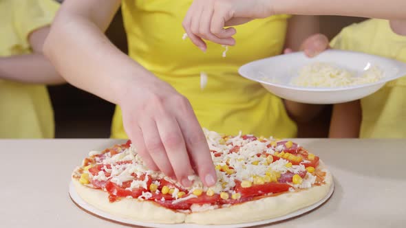 Children Together with Mom Cook Pizza Close Up. The Girls Sprinkle Pizza with Cheese Close-up, and