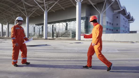 Two Construction Workers in Orange Uniform and Helmets Meeting Each Other at the Bulding Object