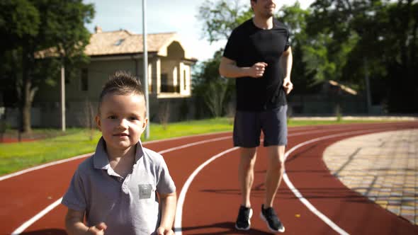 Dad and His Little Son in Sportswear are Smiling and Jogging By Track