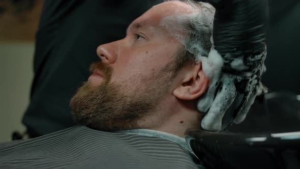 Closeup of Bearded Man Head Washed with Shampoo Foam in a Barbershop
