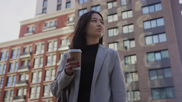 Low Angle Portrait of an Asian Businesswoman on a Modern City Street with Coffee