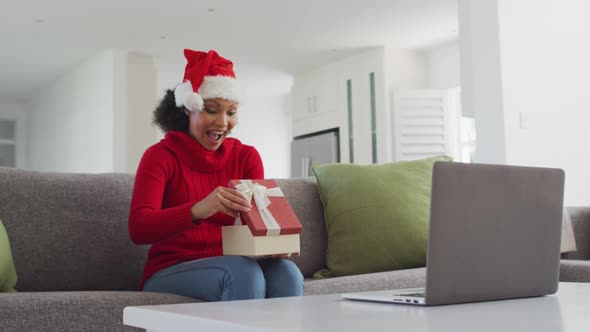 Woman wearing Santa hat opening gift box while having video chat on his laptop