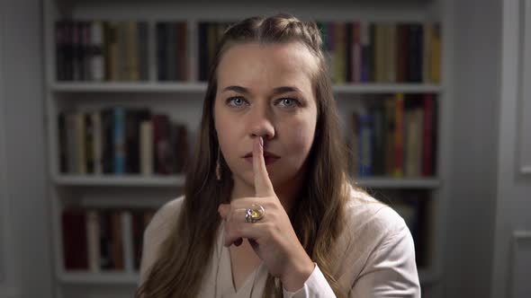Young Lady with Blue Eyes Puts Her Finger To Lips To Make Silence