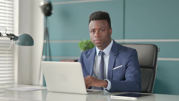 African Businessman Shaking Head As No Sign While Using Laptop in Office