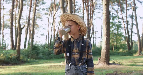 Small Boy in Hat Which Drinking Tea Among Green Park on Sunny day