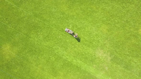 Aerial View of Small Figure of Man Worker Trimming Green Grass with Mowing Mashine on Football