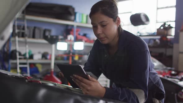 Female mechanic using digital tablet and inspecting the car at a car service station