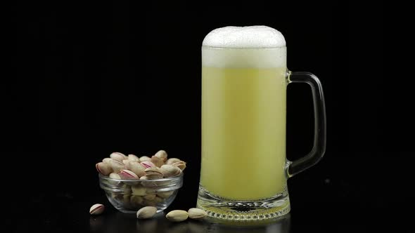 Beer Is Pouring Into Glass on Black Background. Bowl of Pistachios Nuts