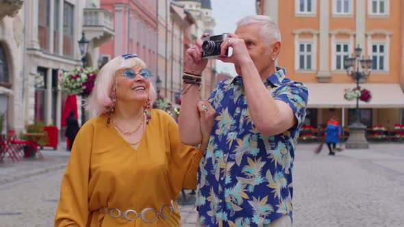 Elderly Stylish Tourists Man and Woman Taking Photos with Old Film Camera Walking Along City Street