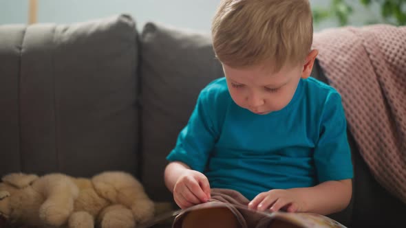 Concentrated Little Boy Looks at Pictures Sitting on Sofa