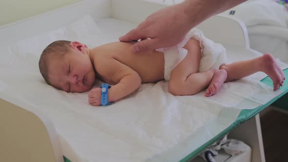 Men hands massage the back of a newborn baby on the changing table in the maternity hospital