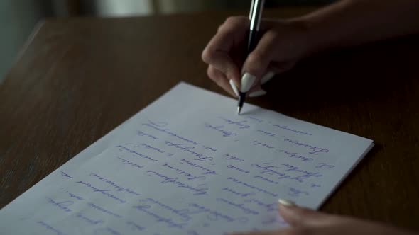 Female hands writing letter on white paper on wooden table close up.  Love bridal vow, calligraphy