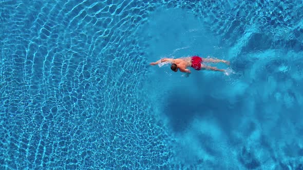 Aerial View of Man in Red Shorts Swims in the Pool