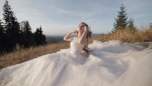 Beautiful and Lovely Bride in Wedding Dress Sitting on Grass on Mountain Slope