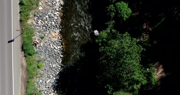 A river flows heavy next to a road as the drone descends cars drive by.  60fps 4k.