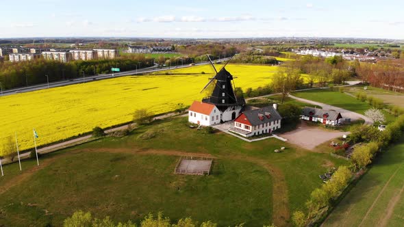 Drone circling windmill from far flying over green field. Sweden springtime