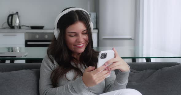 Brunette Woman Listening to Music in Headphones Sitting in the Cozy Sofa