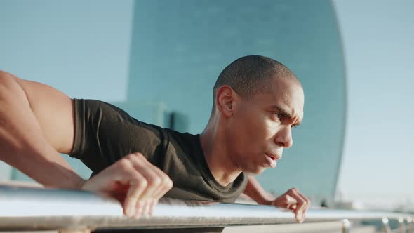 Serious bald sportsman wearing black t-shirt does push-ups from the railing outdoors