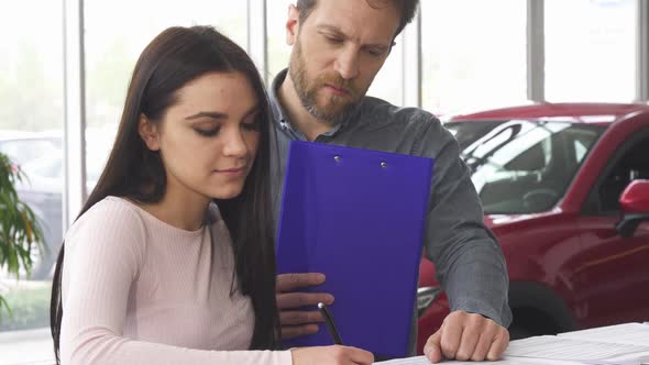 Mature Car Dealer Signing Papers with His Female Customer