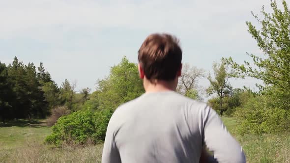 a Young Caucasian Man in Light Sportswear Runs in a Green Park