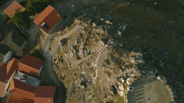 A drone captures a group of tourists hikes up a stone at Folgosinho Castle in a top-down position.