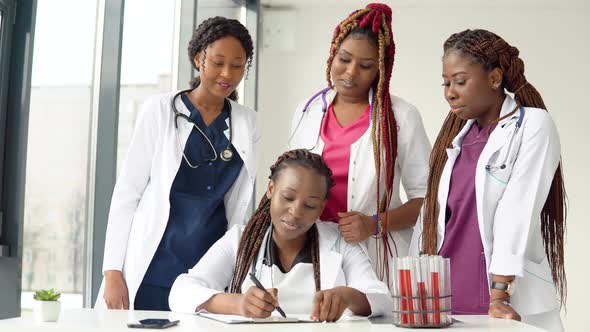 Young Doctors Have a Discussion Standing at a Table While One of Them Makes Notes