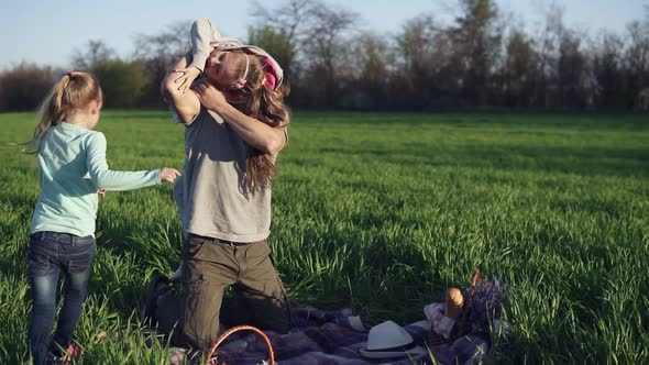 A Young Parent Plays with His Grownup Daughters in a Meadow on a Litter