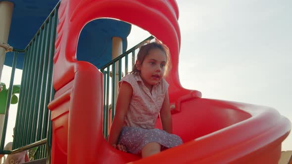 Cute Little Girl Slides Down the Slide at the Playground in Summer