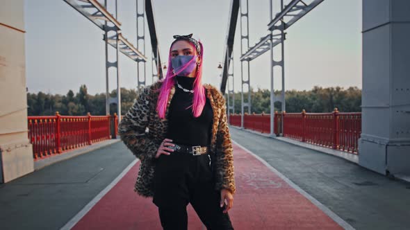 Hipster Lady with Pink Hair in Informal Outfit and Protective Mask is Posing Standing on Bridge with