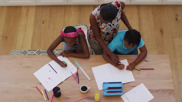 Overhead view of african american mother helping her daughter and son with homework at home