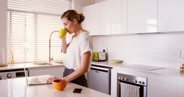 Woman using laptop while having coffee in kitchen