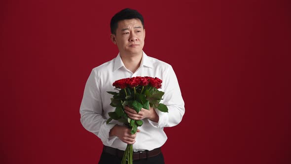 Displeased Asian man in white shirt with a bouquet of red roses waiting for someone