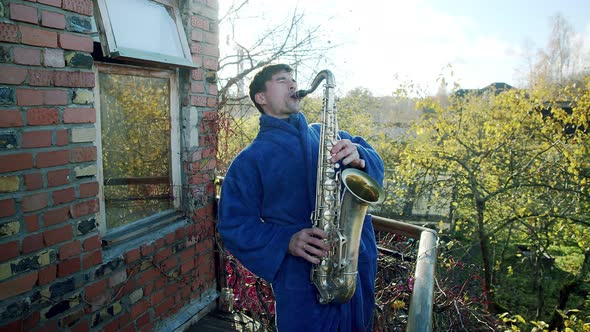 a Man in a Dressing Gown Plays the Saxophone on the Balcony in the Sunlight Having Fun in Quarantine