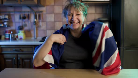 Caucasian adult woman wrapping in nationa british flag and smiling sitting at home.