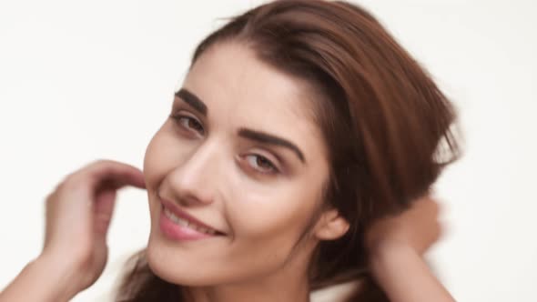 Beautiful Caucasian Female with Long Brown Hair Standing on White Background Touching Combing Hair