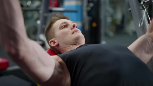 Closeup of Motivated Handsome Sportsman Lifting Barbell Exhaling Lying on Exercise Bench in Gym