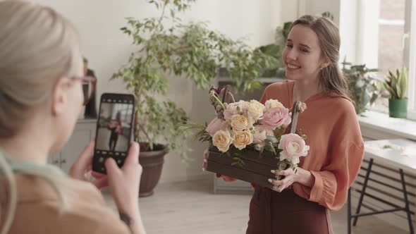 Friend Photographing Woman Holding Flowers Arrangement