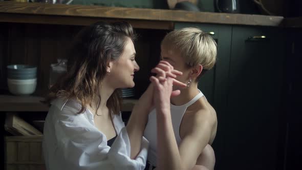 Affectionate Lesbian Couple Hugging and Kissing While Sitting on Kitchen Floor