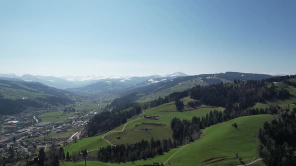 Scenic aerial forward over green hills in Switzerland, with city and mountains.