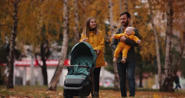 Young Family Walking with Baby Carriage at the Autumn Park